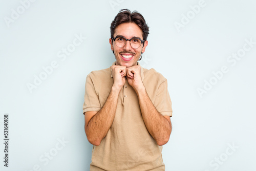 Young hispanic man isolated on blue background keeps hands under chin, is looking happily aside.