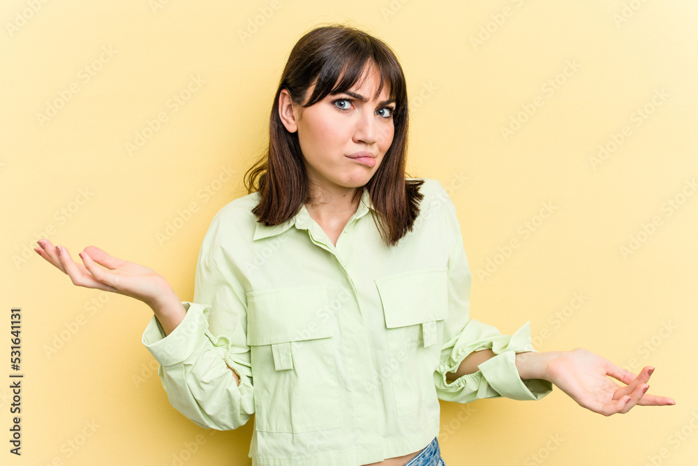 Young caucasian woman isolated on yellow background doubting and shrugging shoulders in questioning gesture.