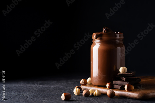 Obraz na plátně Chocolate paste in jar with nuts on cut wooden board