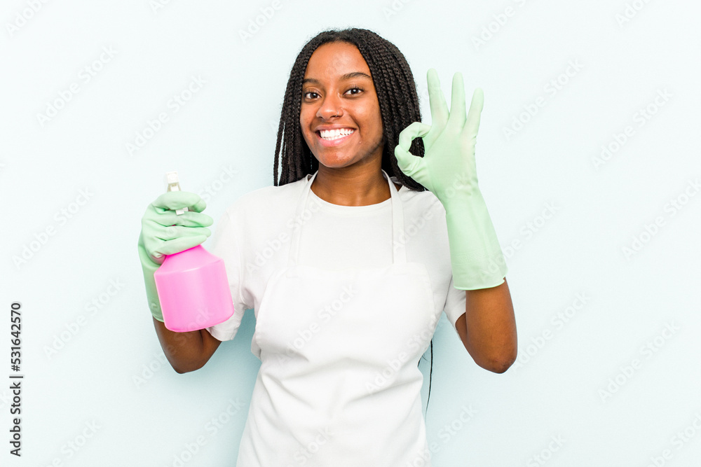 Young African American cleaner woman isolated on blue background cheerful and confident showing ok gesture. Young African American cleaner woman isolated on blue background cheerful and confident showing ok gesture.