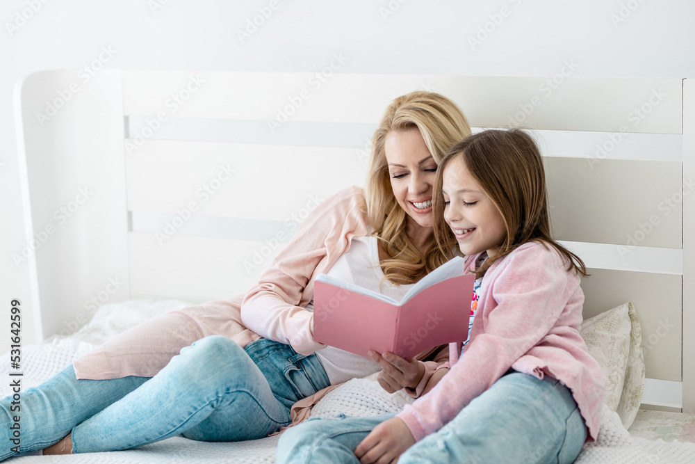 Happy mother with adorable little daughter reeding book on bed Happy mother with adorable little daughter reeding book on bed