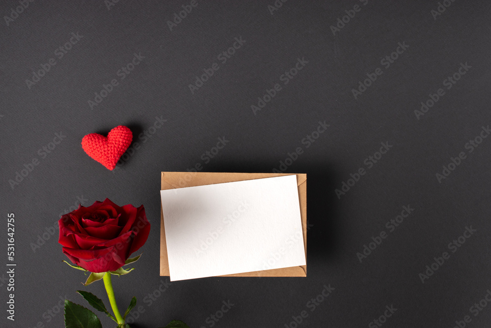 A red rose and a mock-up of a kraft envelope with a blank sheet on a black background. Banner for Valentine's Day. Postcard for February 14. Love. Minimalism. A red rose and a mock-up of a kraft envelope with a blank sheet on a black background. Banner for Valentine's Day. Postcard for February 14. Love. Minimalism.