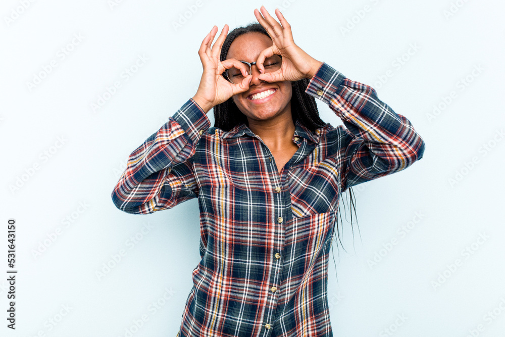 Young African American woman with braids hair isolated on blue background showing okay sign over eyes Young African American woman with braids hair isolated on blue background showing okay sign over eyes