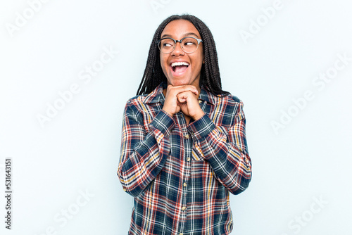 Young African American woman with braids hair isolated on blue background keeps hands under chin, is looking happily aside. © Asier