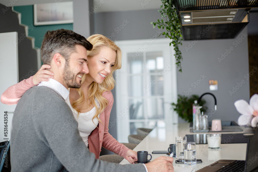 Remote work and freelance. Affectionate woman looking at her boyfriend working on laptop in kitchen and bringing him coffe Remote work and freelance. Affectionate woman looking at her boyfriend working on laptop in kitchen and bringing him coffe