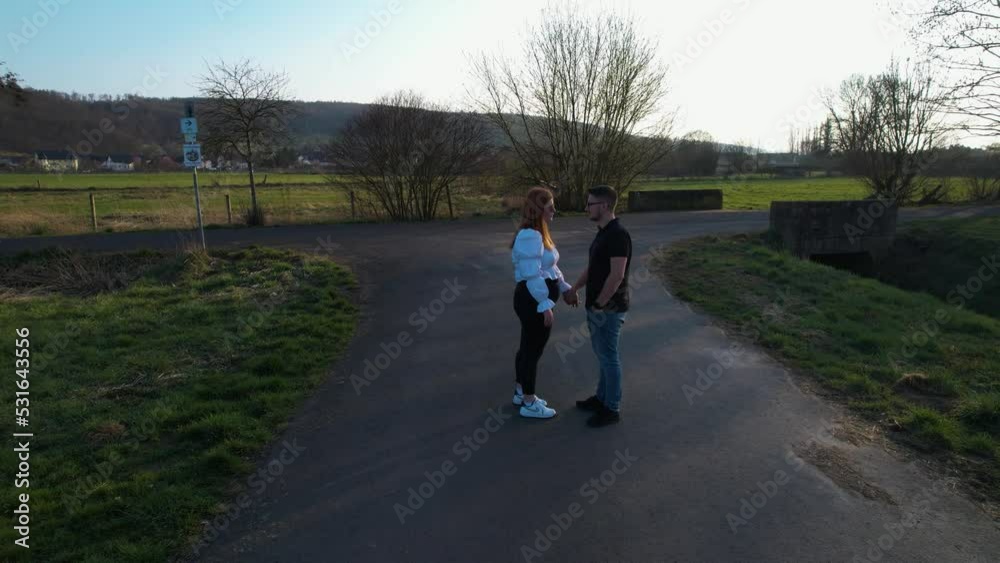 Aerial view around a couple holding hands on a rural road, spring evening in Germany - orbit, drone shot Aerial view around a couple holding hands on a rural road, spring evening in Germany - orbit, drone shot