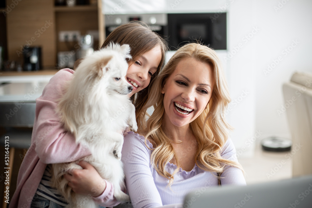 Mother working on laptop in living room, while daughter is interrupting her with dog Mother working on laptop in living room, while daughter is interrupting her with dog