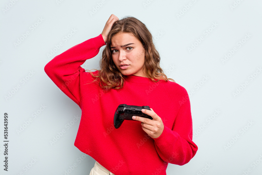 Young caucasian gamer woman holding a game controller isolated on blue background being shocked, she has remembered important meeting. Young caucasian gamer woman holding a game controller isolated on blue background being shocked, she has remembered important meeting.