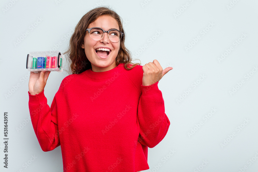 Obraz premium Young caucasian woman holding battery box isolated on blue background points with thumb finger away, laughing and carefree.