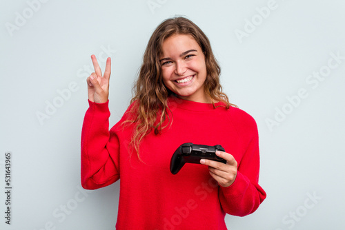 Young caucasian gamer woman holding a game controller isolated on blue background showing number two with fingers.