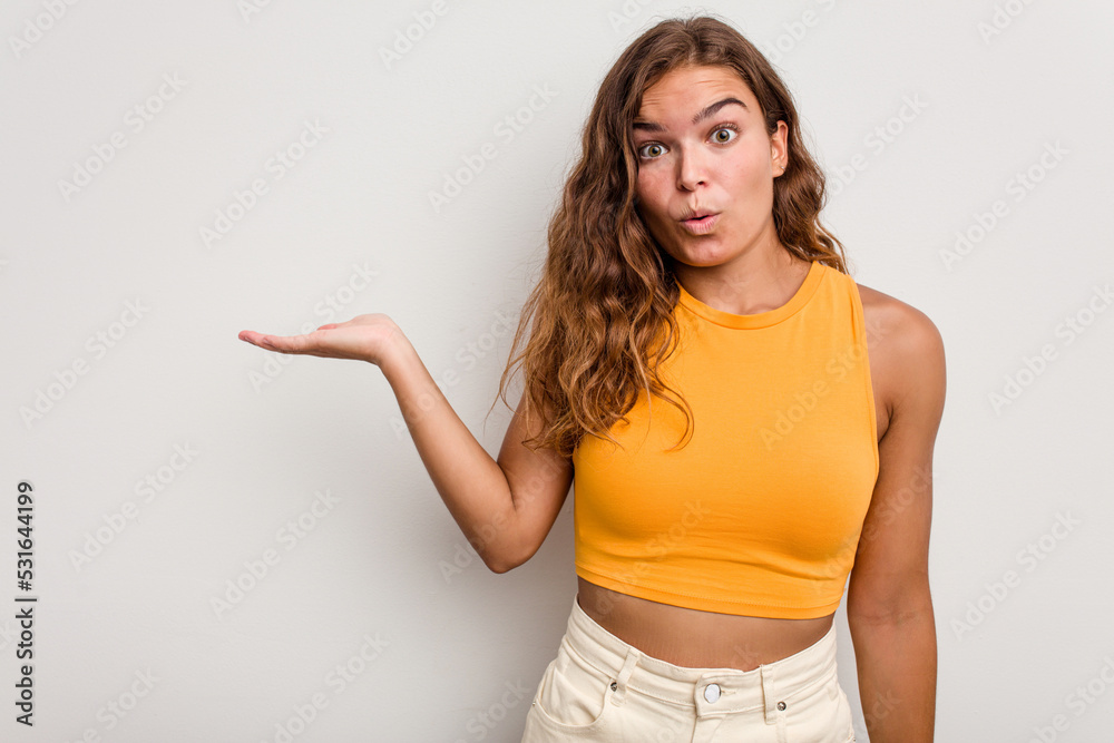 Young caucasian woman isolated on blue background impressed holding copy space on palm. Young caucasian woman isolated on blue background impressed holding copy space on palm.