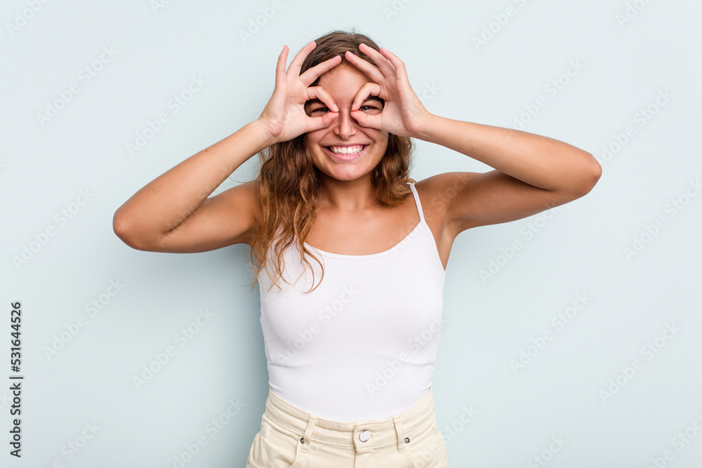 Young caucasian woman isolated on blue background showing okay sign over eyes Young caucasian woman isolated on blue background showing okay sign over eyes
