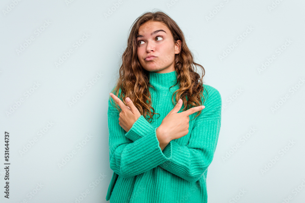 Young caucasian woman isolated on blue background points sideways, is trying to choose between two options. Young caucasian woman isolated on blue background points sideways, is trying to choose between two options.