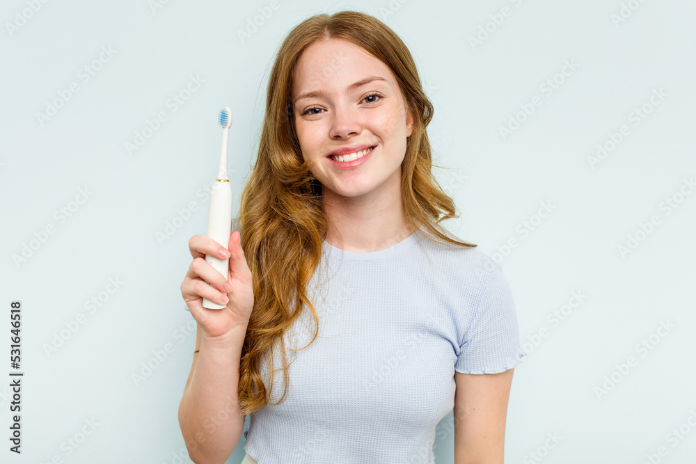 Young caucasian woman holding electric toothbrush isolated on blue background happy, smiling and cheerful. Young caucasian woman holding electric toothbrush isolated on blue background happy, smiling and cheerful.
