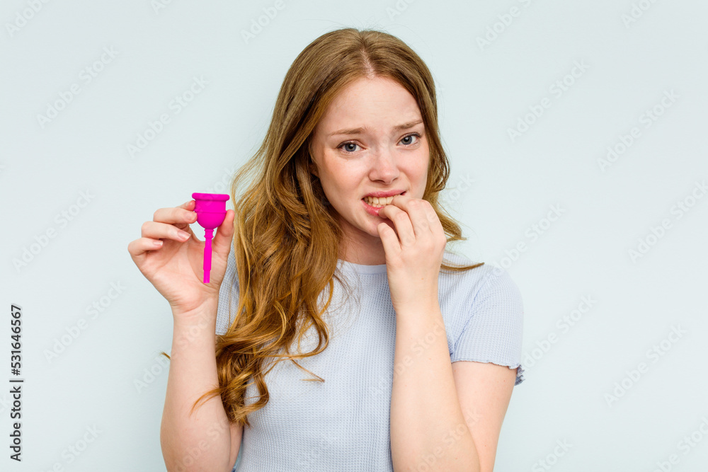 Young caucasian woman holding menstrual cup isolated on blue background biting fingernails, nervous and very anxious. Young caucasian woman holding menstrual cup isolated on blue background biting fingernails, nervous and very anxious.