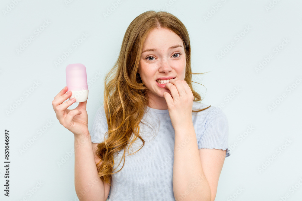 Young caucasian woman holding deodorant isolated on blue background biting fingernails, nervous and very anxious. Young caucasian woman holding deodorant isolated on blue background biting fingernails, nervous and very anxious.