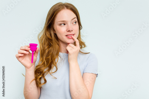 Young caucasian woman holding menstrual cup isolated on blue background relaxed thinking about something looking at a copy space.