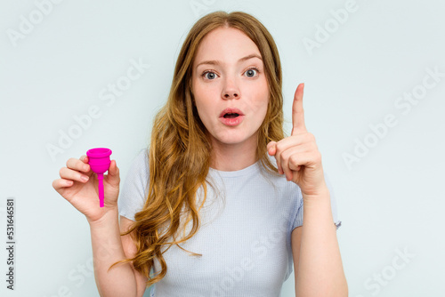 Young caucasian woman holding menstrual cup isolated on blue background having an idea, inspiration concept.