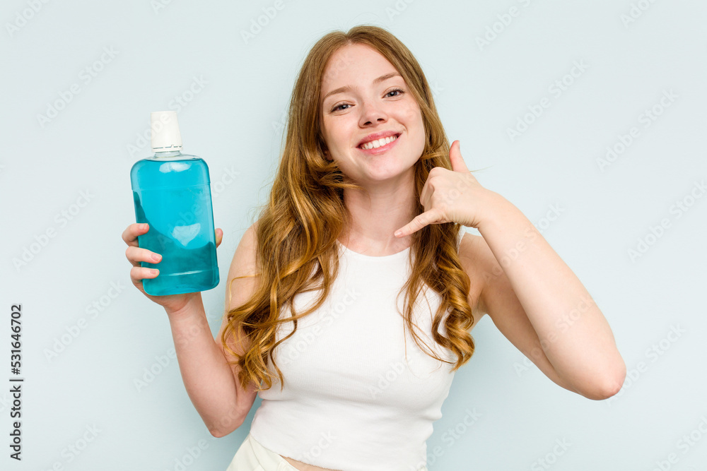 Young caucasian woman holding a mouthwash isolated on blue background showing a mobile phone call gesture with fingers. Young caucasian woman holding a mouthwash isolated on blue background showing a mobile phone call gesture with fingers.