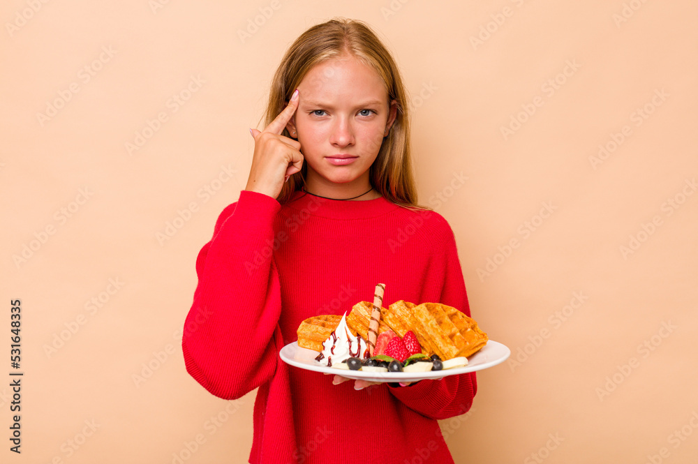Little caucasian girl holding a waffles isolated on beige background showing a disappointment gesture with forefinger.
