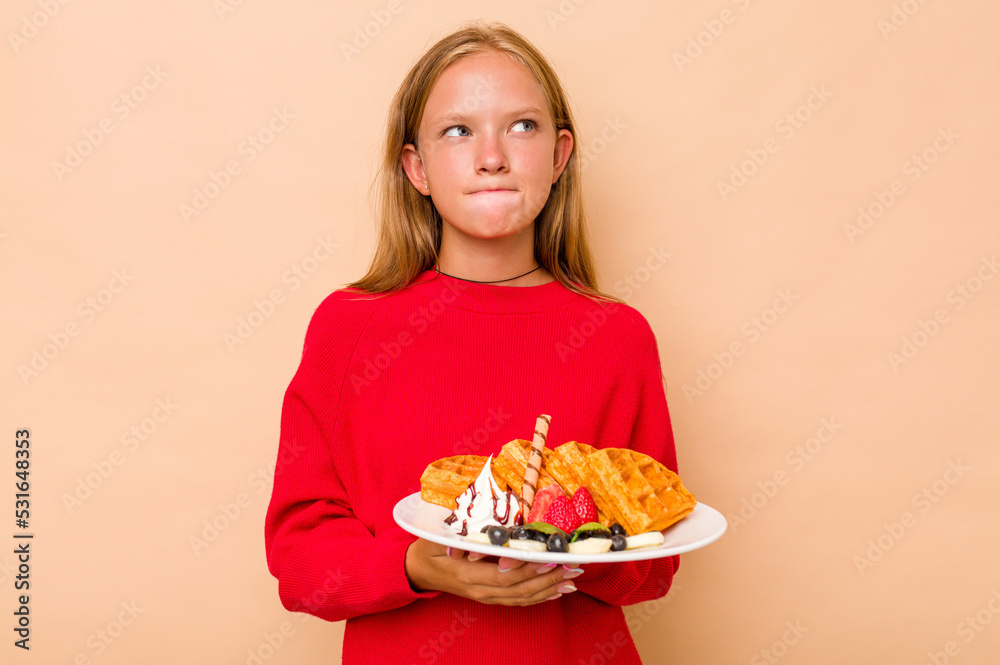 Little caucasian girl holding a waffles isolated on beige background confused, feels doubtful and unsure. Little caucasian girl holding a waffles isolated on beige background confused, feels doubtful and unsure.