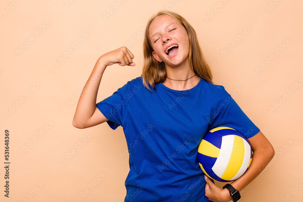 Little caucasian girl playing volleyball isolated on beige background raising fist after a victory, winner concept.
