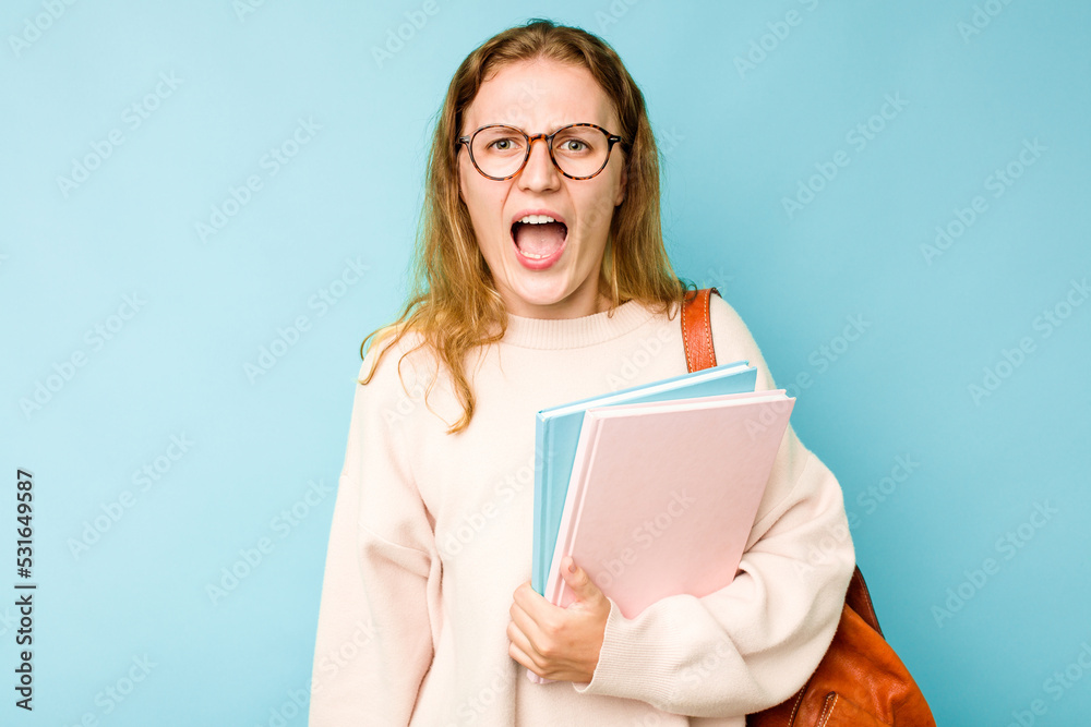 Young student caucasian woman isolated on blue background screaming very angry and aggressive. Young student caucasian woman isolated on blue background screaming very angry and aggressive.