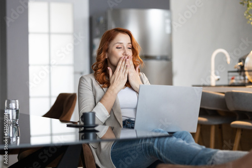 Shot of a young woman using her laptop in kitchen for video call sending kisses. Comfort of home full of smile and happiness. Relaxed time with cup of coffee