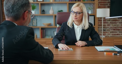 Unknown bearded corrupt businessman giving bribe to confident blonde law abiding businesswoman,she,in turn,refuses the money,corruption concept