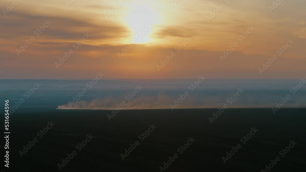 Landscape with a setting sun and a tractor tilling the soil. Orange sky, dust coming from tractor. plow tillage. Cinematic frame. 4К Landscape with a setting sun and a tractor tilling the soil. Orange sky, dust coming from tractor. plow tillage. Cinematic frame. 4К