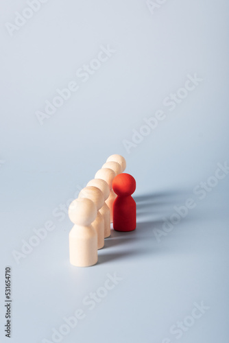 Selective focus on a red wooden figure that stands apart from other identical figures. The concept of protest, group, assembly, distinctive features of the individual.