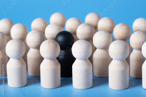 Selective focus on a black figure that stands among identical wooden figures. The concept of a meeting, a crowd, a group