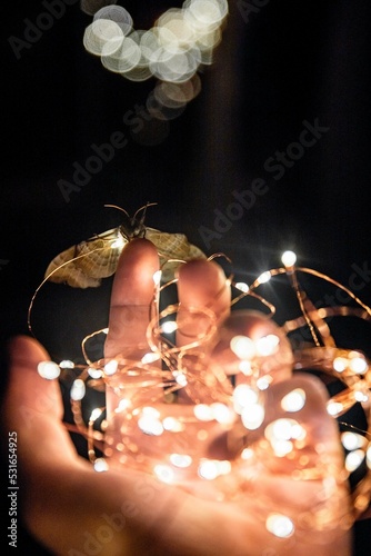 On an abstract light background, a close-up of a hand holding a light bulb and Christmas decorations
