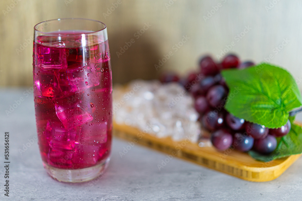 Refreshing a glass of grape juice with ice cubes on wooden tray Refreshing a glass of grape juice with ice cubes on wooden tray