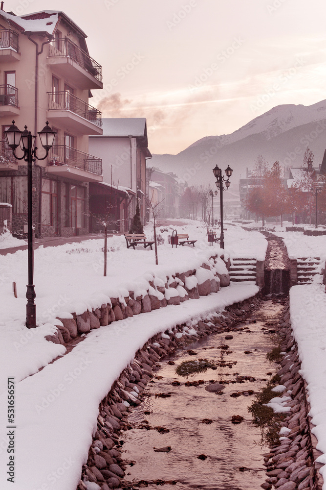Bansko, Bulgaria, Gotse Delchev street view with old, traditional houses, water stream and Pirin mountains