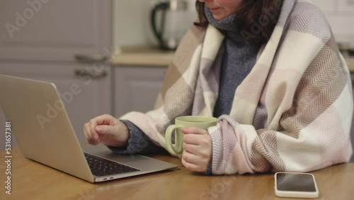 frozen woman sit kitchen wrapped warm blanket warm hands hold cup working laptop. concept cold heating off in apartment high prices home utilities heating shutdown bankruptcy. female cold hands typing photo