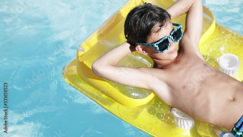 4k video Portrait of handsome boy in sunglasses in swimming pool on air matrass, child enjoying swimming in summer in pool. Vacation hotel concept.