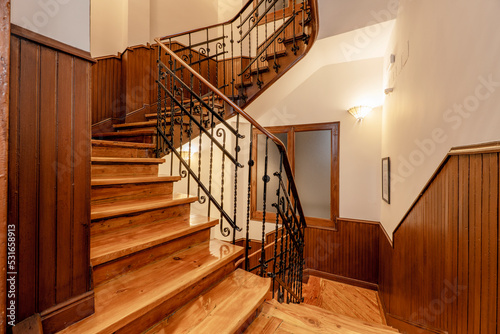 Landing between floors of a vintage building with pine wood stairs and metal railing