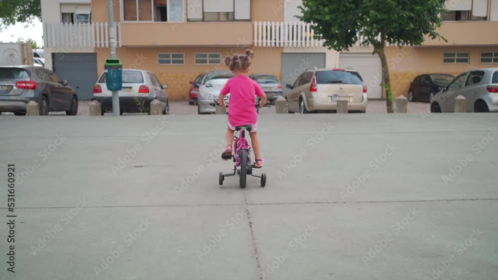 Cute little smiling girl riding bike bicycle in city on parking sunny summer day. Active family leisure with kids. Little caucasian girl 5 years old have fun with pink child bicycle Cute little smiling girl riding bike bicycle in city on parking sunny summer day. Active family leisure with kids. Little caucasian girl 5 years old have fun with pink child bicycle