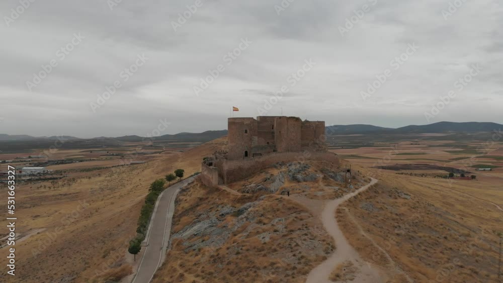 Aerial rising up shot in front of an old medieval stone castle, a fort with bastions, towers guarding the land, white windmills in the background. Aerial rising up shot in front of an old medieval stone castle, a fort with bastions, towers guarding the land, white windmills in the background.