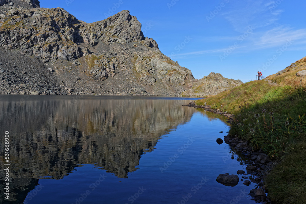 REVEL, FRANCE, August 24, 2022 : Hiker admires the view of eraly morning lights on blue mountain lake called Lac du Petit Domenon. REVEL, FRANCE, August 24, 2022 : Hiker admires the view of eraly morning lights on blue mountain lake called Lac du Petit Domenon.