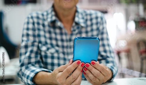 Elderly woman in checkered shirt sitting at indoor cafe table using mobile phone to read a message