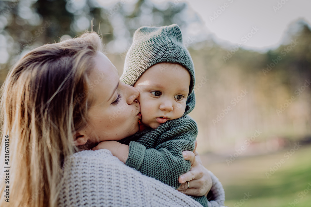 Obraz premium Mother holding and kissing her little baby son wearing knitted sweater during walk in nature, close-up
