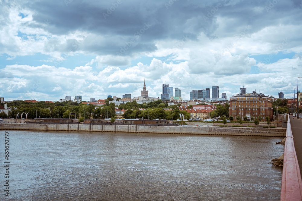 Obraz premium Cloudy day of the big city in Warsaw in summer, Poland skyscrapers of tall buildings on the horizon above the surface of the Vistula river. city ​​panorama beautiful cityscape