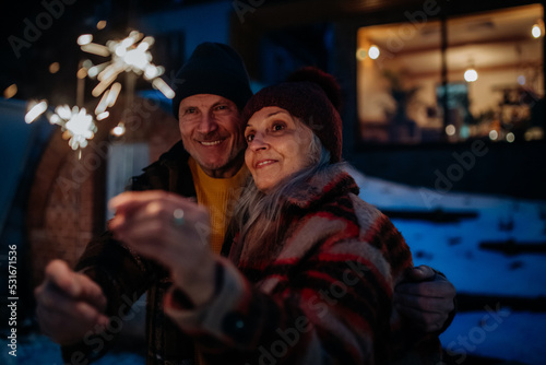 Happy senior couple celebrating new year with sparklers, enjoying winter evening.