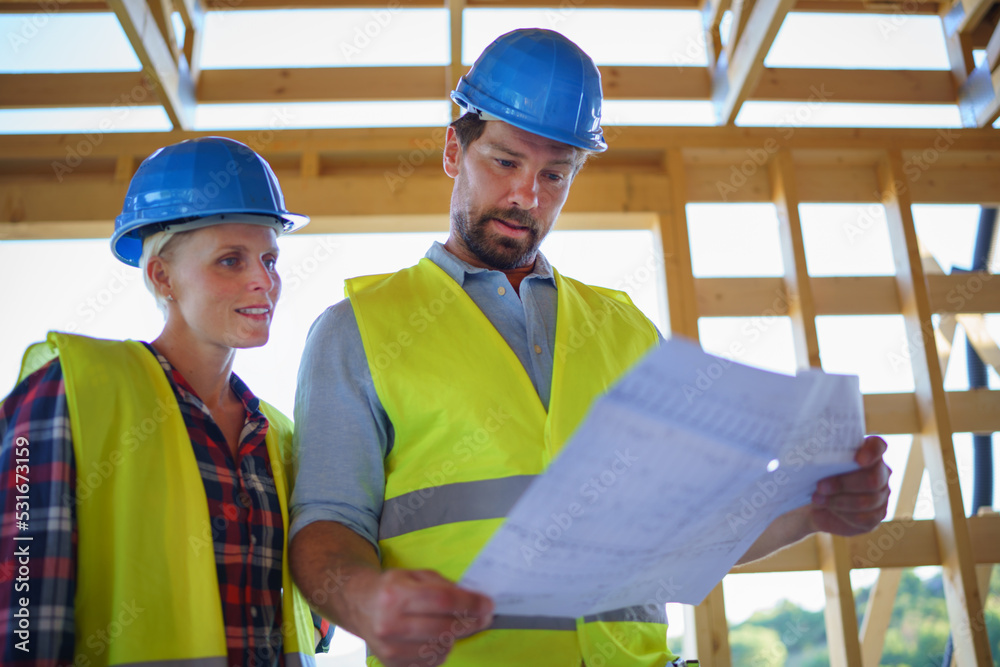 Construction engineers or architects with blueprints checking eco building site of wood frame house Construction engineers or architects with blueprints checking eco building site of wood frame house