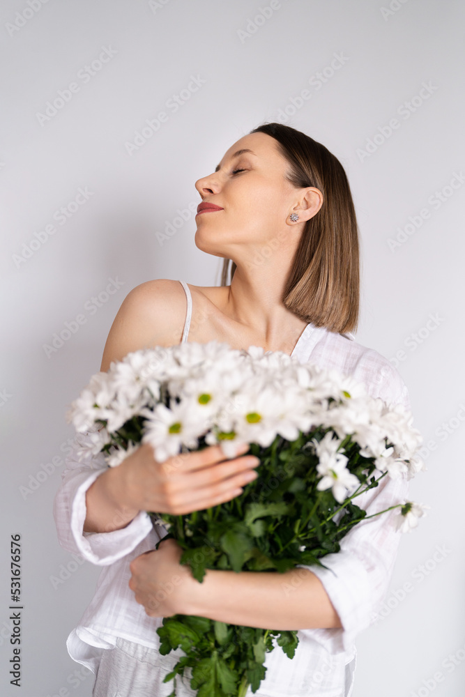 Young beautiful cute sweet lovely smiling woman with hold a bouquet of white fresh flowers on white wall background