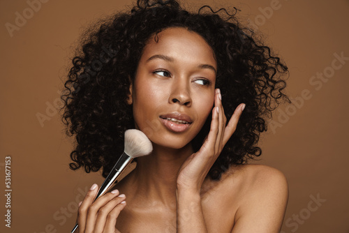 Shirtless black woman looking aside while posing with powder brush
