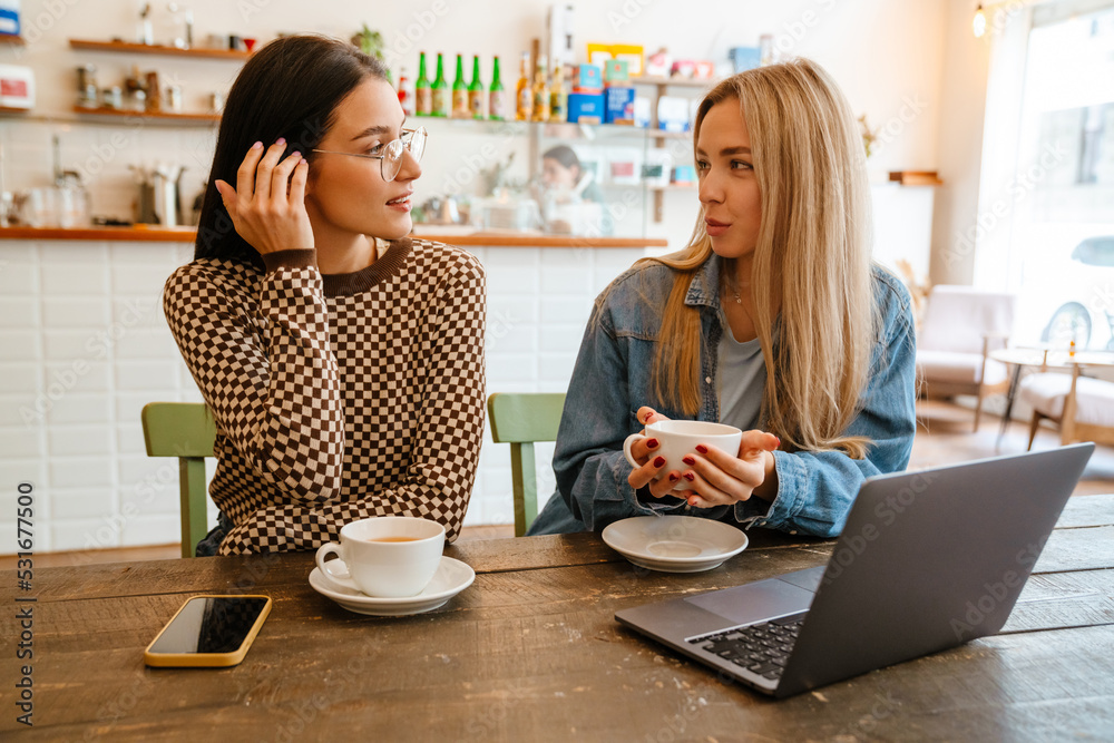 White women talking and using laptop while drinking tea in cafe White women talking and using laptop while drinking tea in cafe