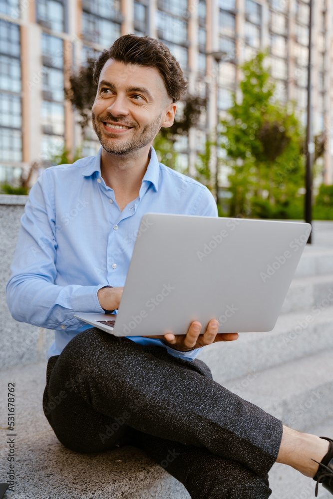 Bristle man working with laptop while sitting on stone bench Bristle man working with laptop while sitting on stone bench